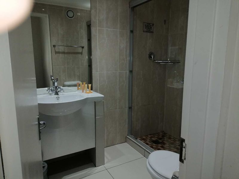 A functional bathroom featuring a vanity basin, tiled shower enclosure with glass door, and a toilet, finished with neutral wall and floor tiles.