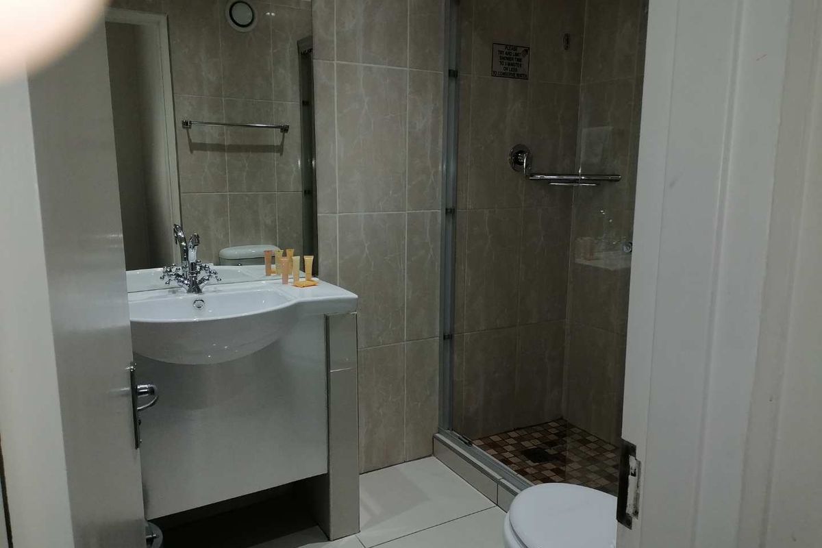 A functional bathroom featuring a vanity basin, tiled shower enclosure with glass door, and a toilet, finished with neutral wall and floor tiles.