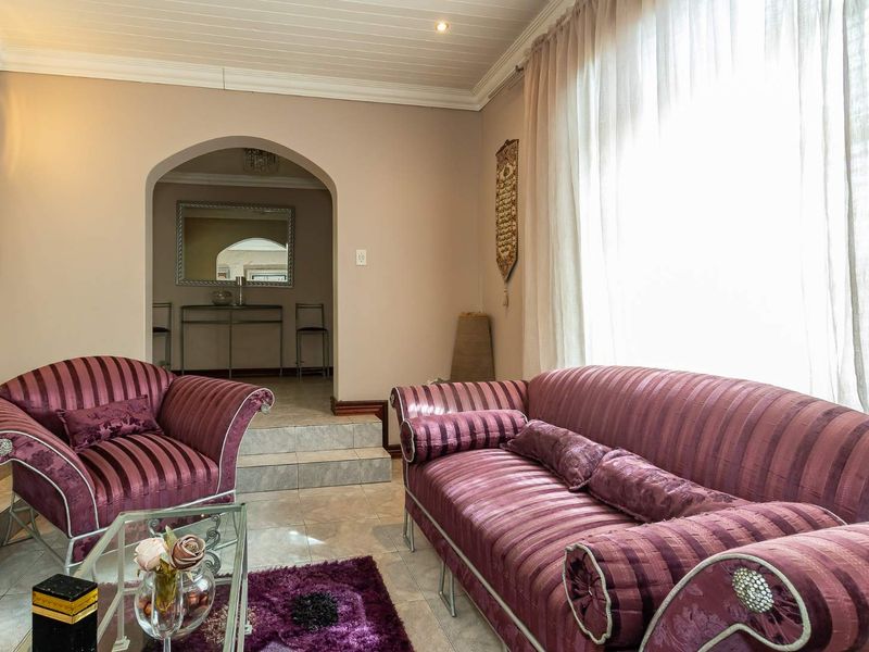 A comfortable living room featuring tiled flooring, an arched doorway leading to an adjacent space, and a classic tongue and groove ceiling.