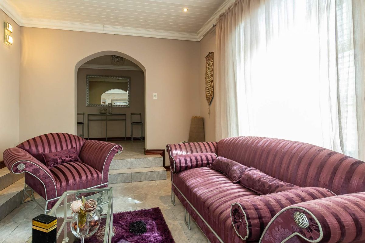 A comfortable living room featuring tiled flooring, an arched doorway leading to an adjacent space, and a classic tongue and groove ceiling.