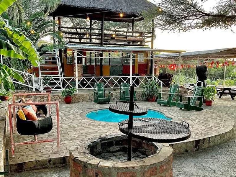 Outdoor entertainment area featuring a swimming pool, stone-paved patio, built-in braai, and a two-story thatched roof structure with overhead string lighting.