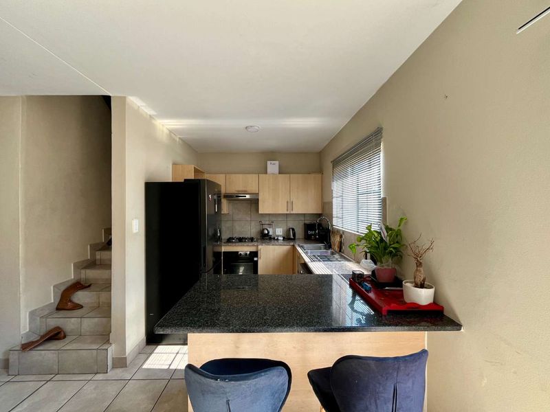 Compact kitchen featuring granite countertops, built-in oven, hob, extractor fan, and light wood cabinetry, with an integrated breakfast bar and adjacent staircase.
