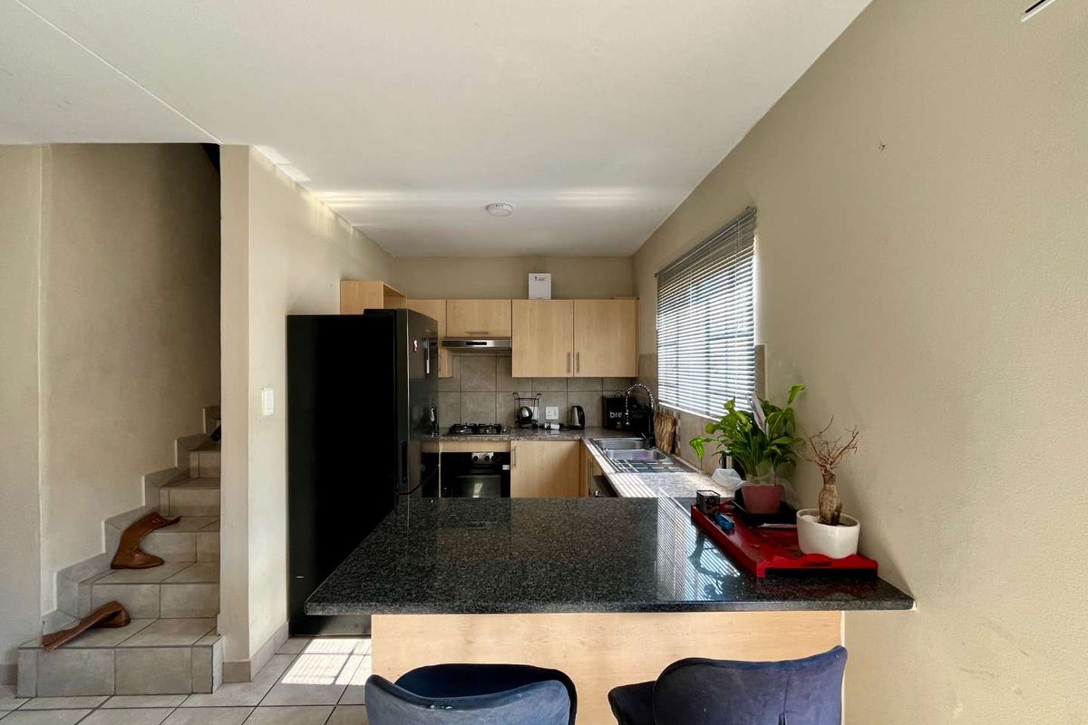 Compact kitchen featuring granite countertops, built-in oven, hob, extractor fan, and light wood cabinetry, with an integrated breakfast bar and adjacent staircase.