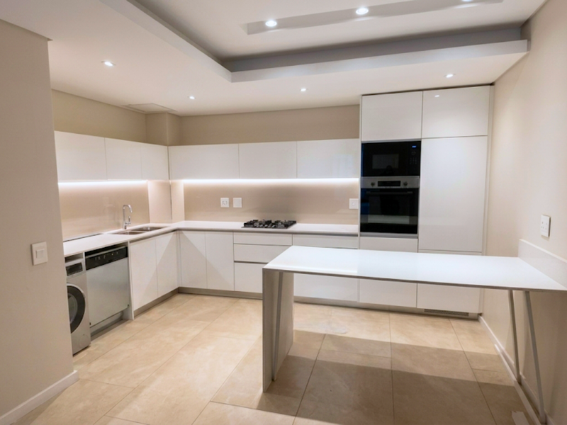 Modern kitchen featuring sleek white cabinetry, integrated appliances, stone countertops, a breakfast bar, and recessed lighting in a clean, contemporary open-plan layout.