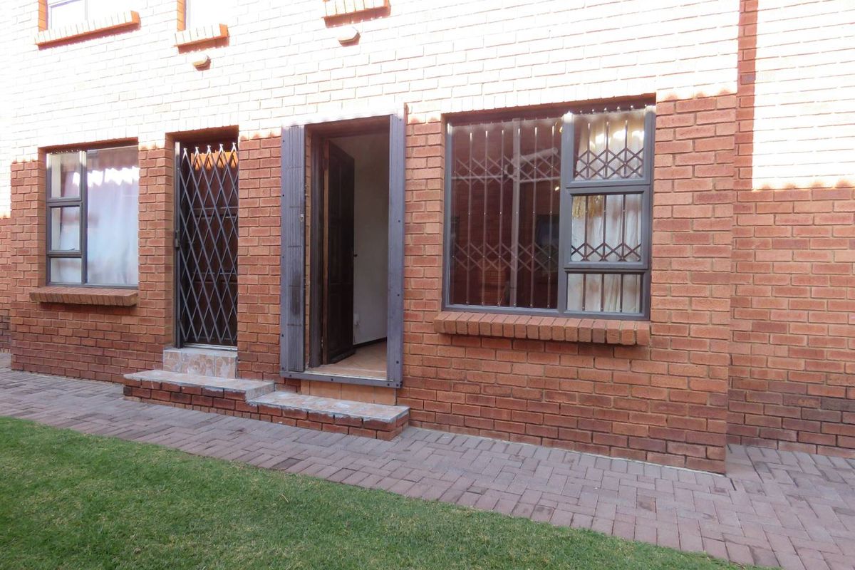 Rear view of a townhouse featuring face-brick exterior, security gates on doors and windows, and a paved walkway leading to the entrance.