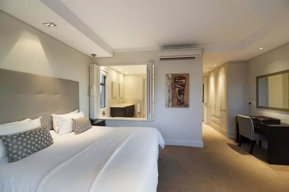 Spacious bedroom featuring neutral carpeting, built-in cabinetry, recessed ceiling lighting, and an integrated air conditioning unit with an open-plan view into the en-suite bathroom.