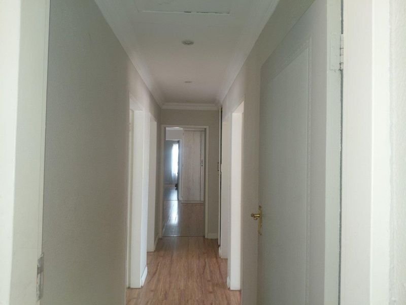 A clean, neutral hallway featuring laminate flooring, recessed downlighting, and coving, providing access to multiple rooms within the home.