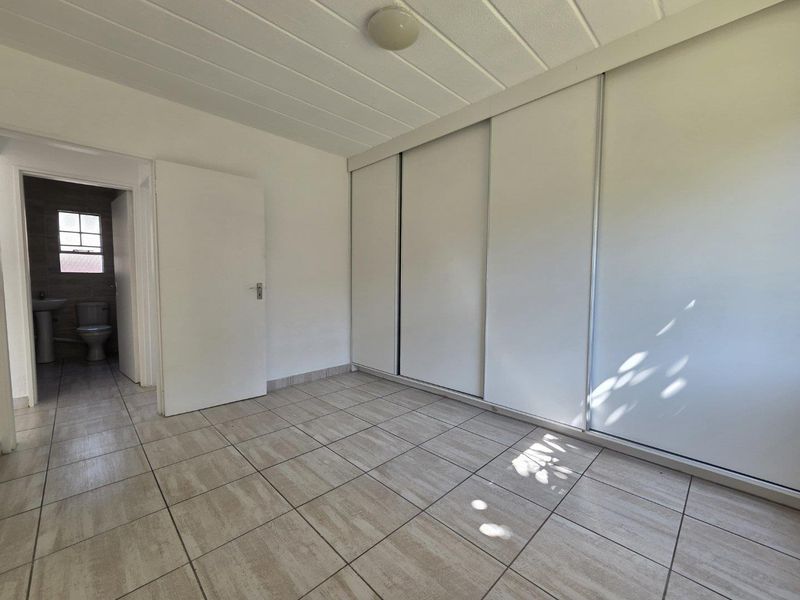 A bright, empty bedroom featuring tiled flooring, a built-in sliding door wardrobe, and direct access to an en-suite bathroom.