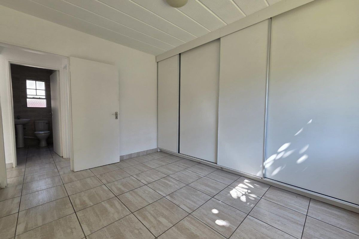 A bright, empty bedroom featuring tiled flooring, a built-in sliding door wardrobe, and direct access to an en-suite bathroom.