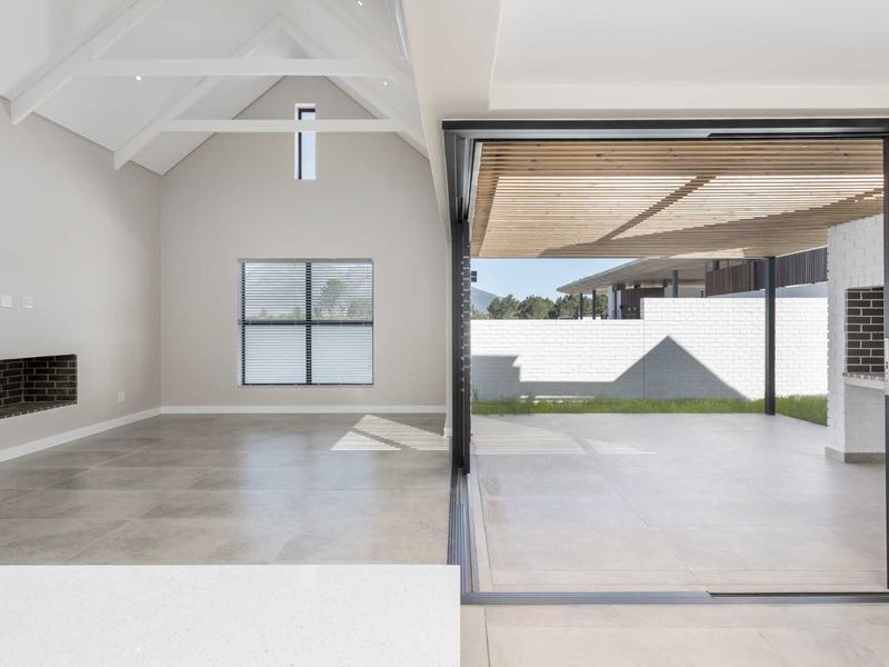 Spacious open-plan living area featuring a vaulted ceiling, built-in fireplace, and seamless transition to a covered patio with a timber pergola.