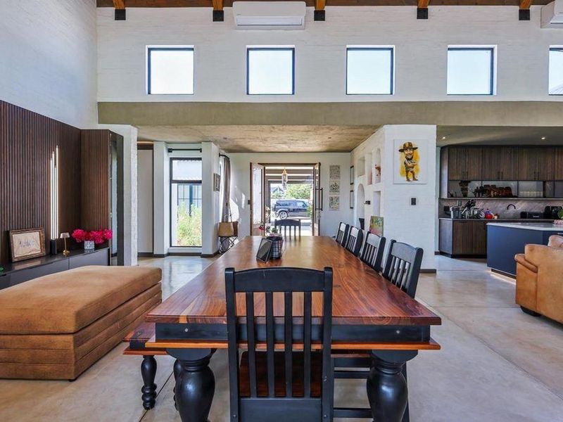 Spacious open-plan living and dining area featuring high ceilings with exposed beams, polished concrete floors, and a modern kitchen with integrated cabinetry.