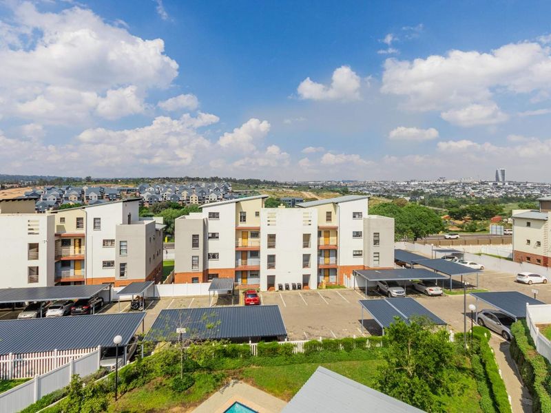 Aerial view of an apartment complex featuring multiple residential blocks, covered parking bays, landscaped grounds, and a swimming pool.