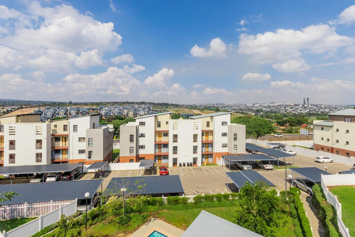 Aerial view of an apartment complex featuring multiple residential blocks, covered parking bays, landscaped grounds, and a swimming pool.