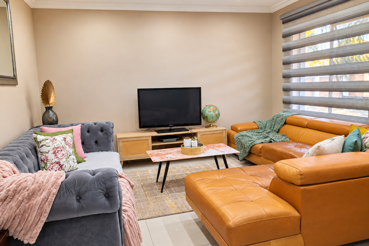 A well-maintained living room featuring neutral wall tones, tiled flooring, recessed downlighting, and modern roller blinds.
