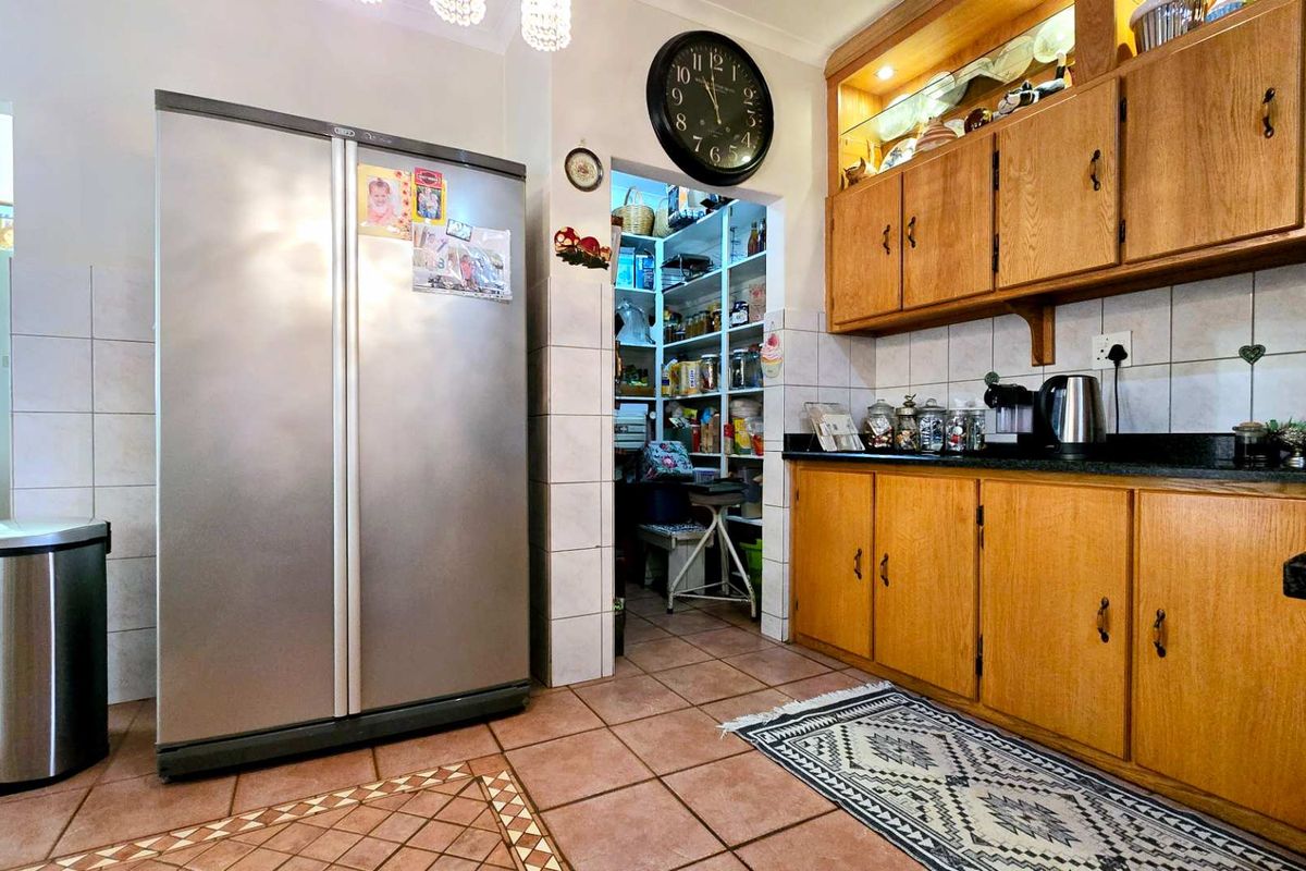 A functional kitchen featuring wooden cabinetry, dark countertops, tiled flooring, and an adjacent walk-in pantry area.