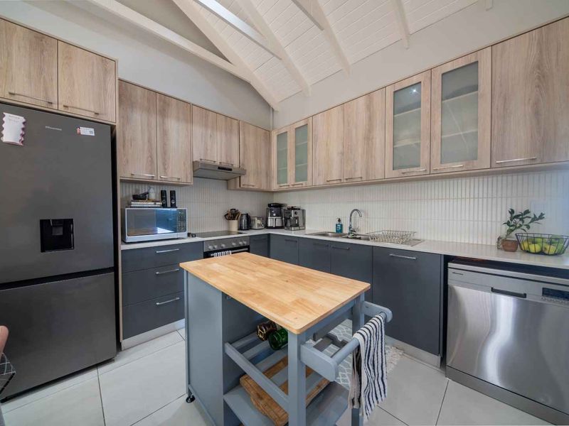 Modern kitchen featuring two-tone cabinetry, stone countertops, tiled backsplash, and a vaulted ceiling, providing a clean and functional culinary space.