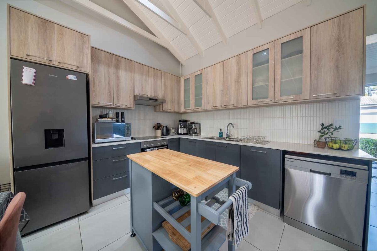 Modern kitchen featuring two-tone cabinetry, stone countertops, tiled backsplash, and a vaulted ceiling, providing a clean and functional culinary space.