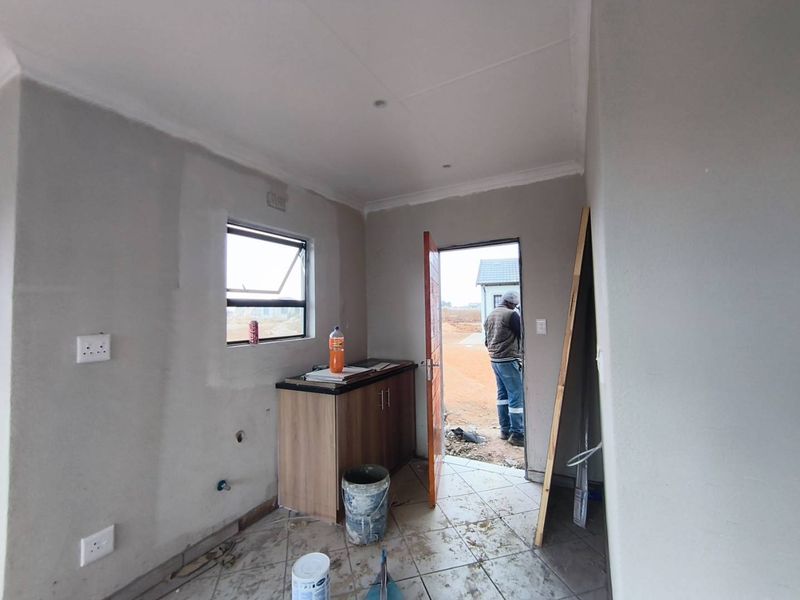 An unfinished kitchen area featuring basic cabinetry, tiled flooring, and plumbing connections, currently in the final stages of construction.