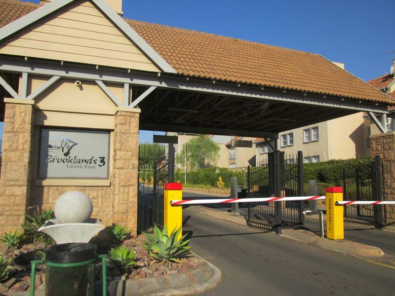 The secure entrance gate of Brooklands 3 Lifestyle Estate, featuring stone-clad pillars, a tiled roof structure, and automated boom gate access control.