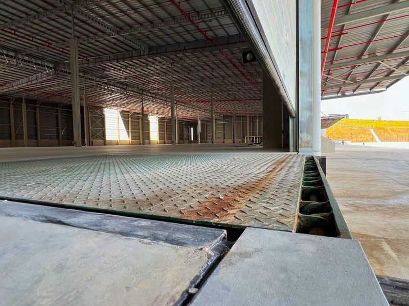 Spacious industrial warehouse interior featuring a dock leveller, high-clearance steel structure, and integrated fire sprinkler system, suitable for logistics or manufacturing operations.
