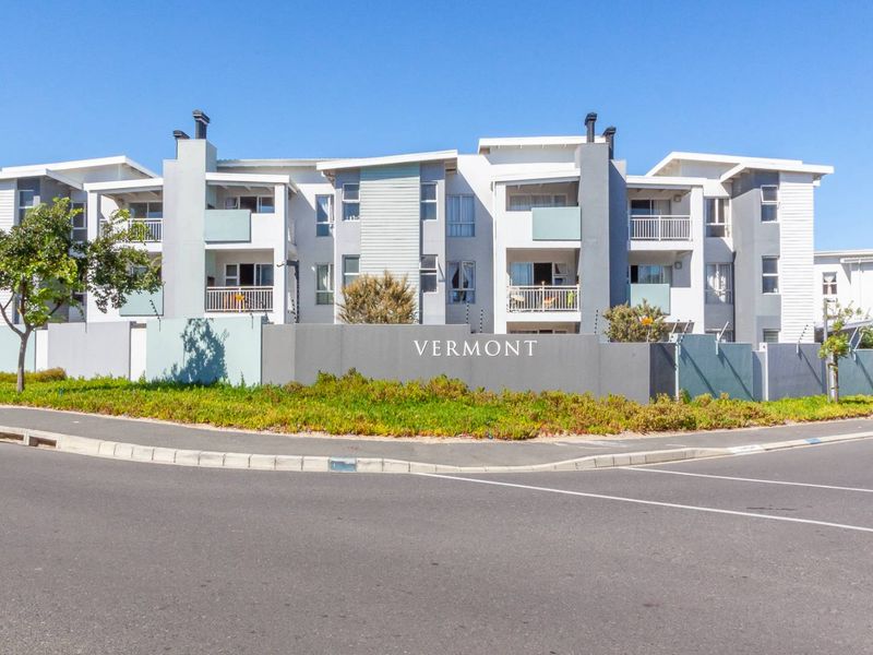 Front exterior view of the Vermont apartment complex, featuring modern multi-story architecture, private balconies, and a secure perimeter wall with electric fencing.