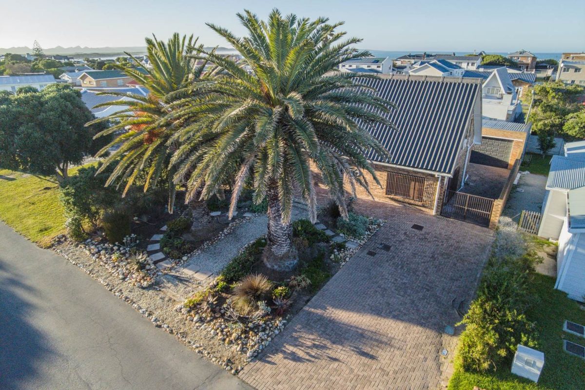 Aerial view of the property featuring a paved driveway, established palm trees, and a corrugated metal roof, situated in a coastal residential neighborhood.