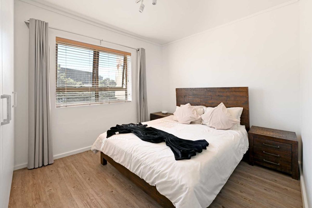 A well-maintained bedroom featuring timber-look laminate flooring, a built-in wardrobe, and natural light through a window fitted with venetian blinds.