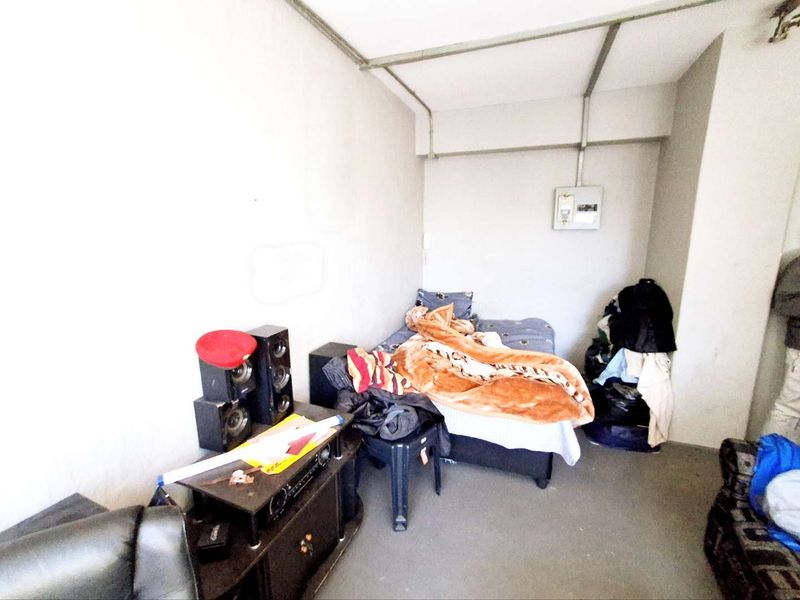 A compact bedroom featuring exposed electrical conduit and a wall-mounted distribution board, requiring cosmetic updates to improve the overall finish.