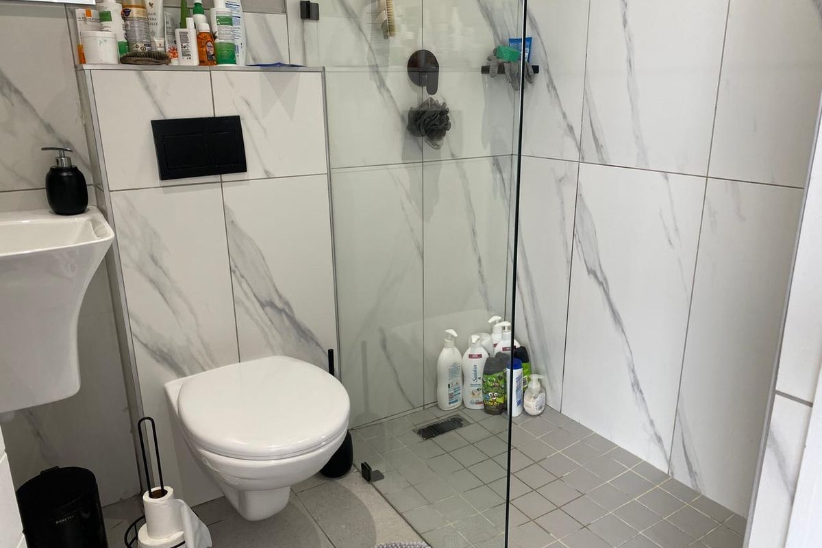 Modern bathroom featuring a wall-mounted toilet, a walk-in shower with glass partition, and marble-effect wall tiling.