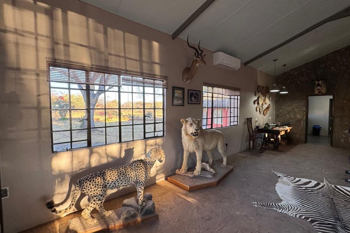 Spacious living area featuring a stone accent wall, exposed beam ceiling, split-system air conditioning, and large steel-framed windows overlooking the surrounding landscape.