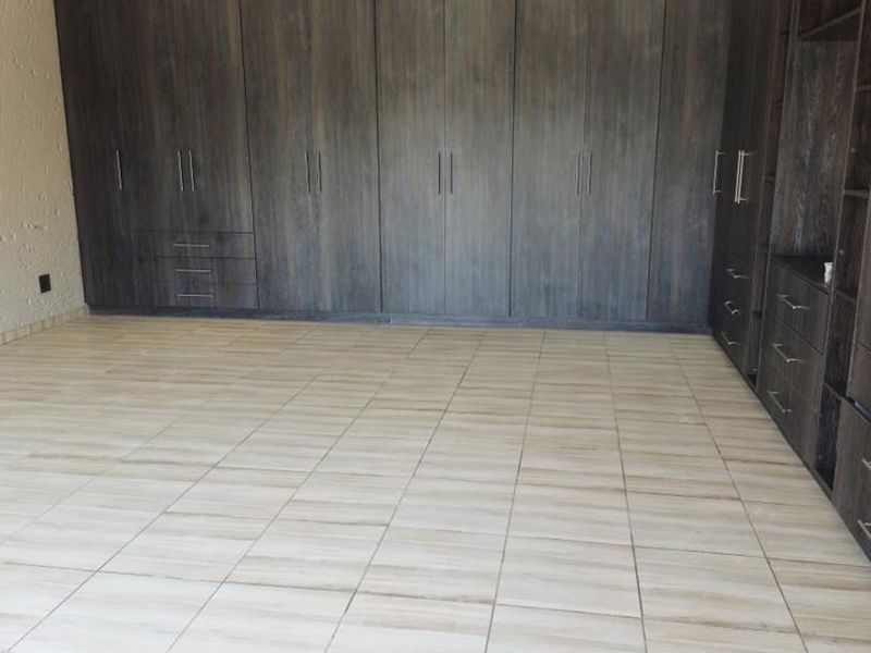 Spacious bedroom featuring extensive dark wood built-in cupboards, neutral tiled flooring, and recessed ceiling lighting.