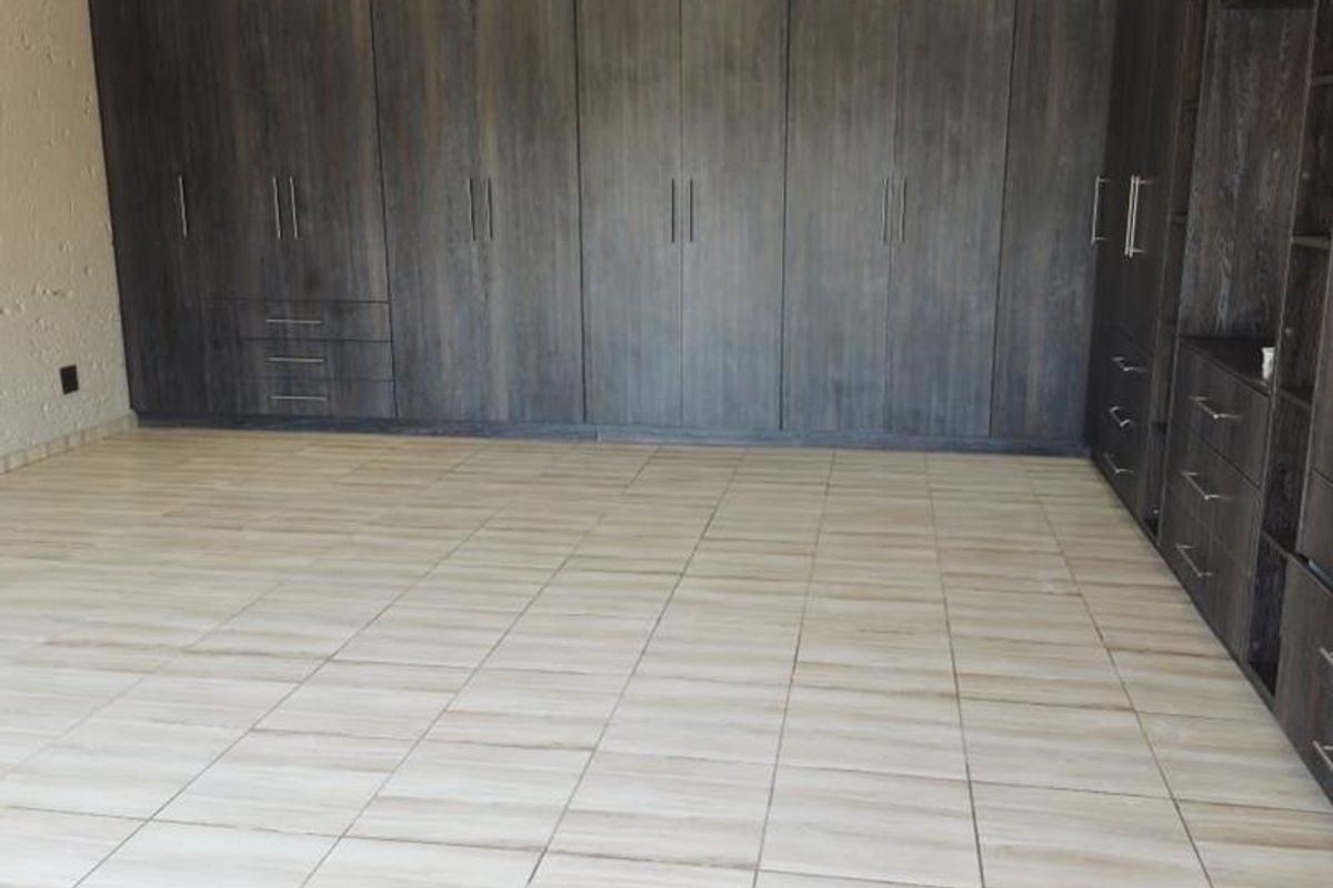 Spacious bedroom featuring extensive dark wood built-in cupboards, neutral tiled flooring, and recessed ceiling lighting.