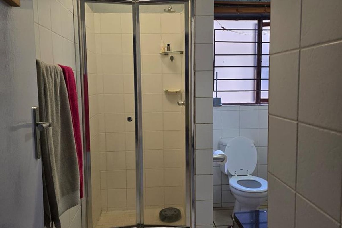 A functional bathroom featuring a glass-enclosed shower, tiled flooring, and a standard toilet, providing essential amenities in a compact layout.