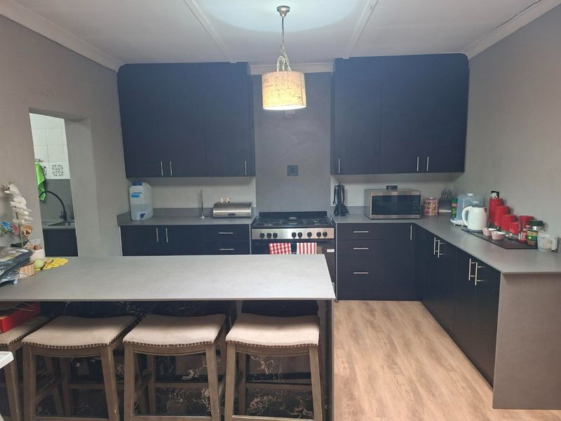 Modern kitchen featuring dark cabinetry, a central island, gas stove, and light wood-look laminate flooring.
