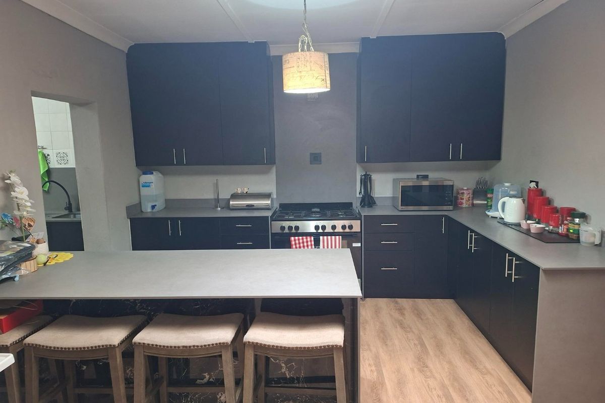 Modern kitchen featuring dark cabinetry, a central island, gas stove, and light wood-look laminate flooring.