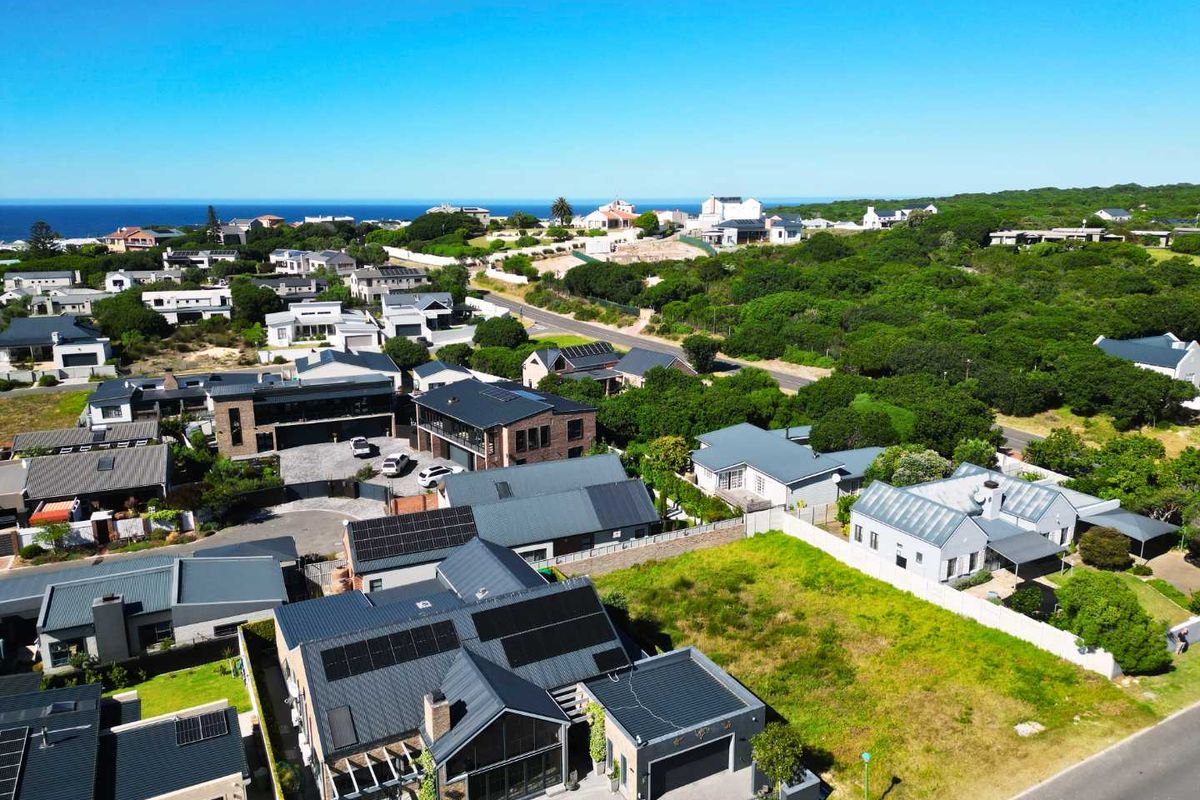 Aerial view of a residential neighborhood featuring modern homes with solar installations, paved driveways, and surrounding coastal landscape.