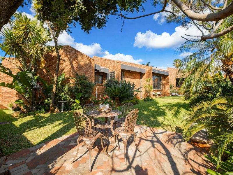 A well-maintained rear garden featuring a brick facade, paved patio area, and established landscaping.