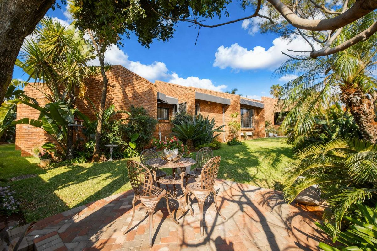 A well-maintained rear garden featuring a brick facade, paved patio area, and established landscaping.