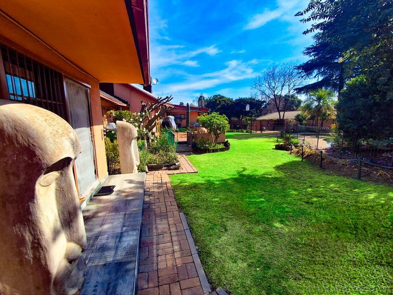 A view of the rear garden featuring a paved walkway, covered patio area, and well-maintained lawn with perimeter fencing.