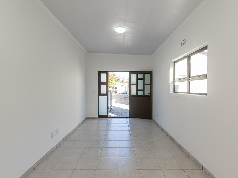 A bright, empty entrance hall featuring neutral tiled flooring, clean white walls, and a glass-paneled door leading to the exterior.