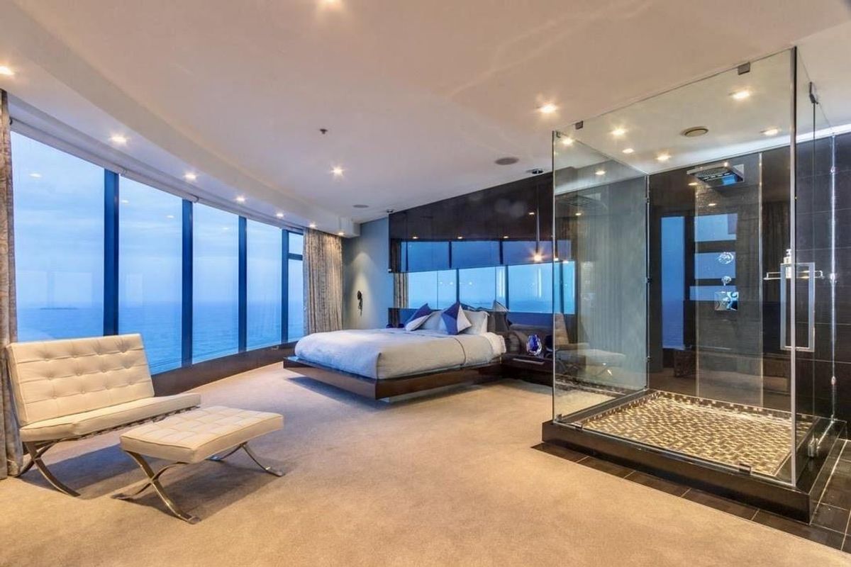 Luxurious open-plan master bedroom suite featuring floor-to-ceiling windows with ocean views, integrated glass-enclosed shower, and high-end modern finishes.