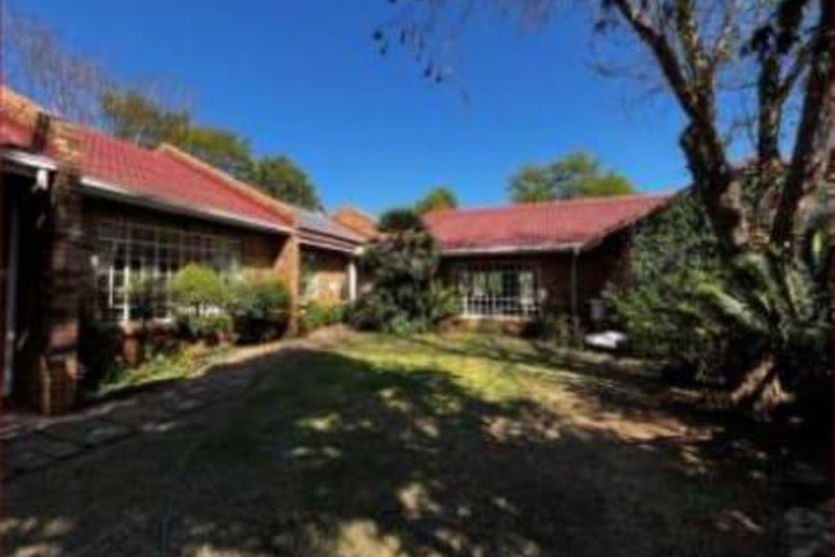 A rear view of the house featuring a red metal roof, brick exterior walls, and a paved walkway leading through the garden area.