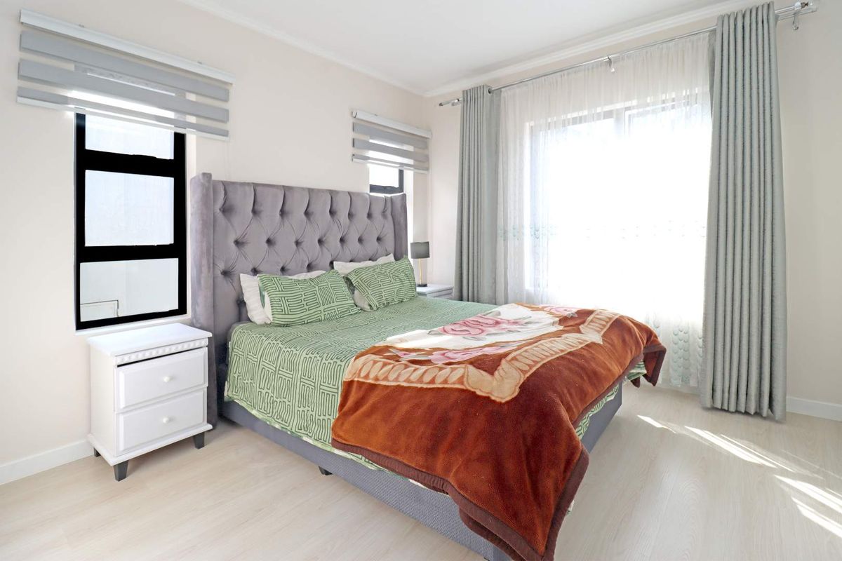 A bright and well-maintained bedroom featuring light laminate flooring, modern aluminium window frames, and neutral wall finishes.