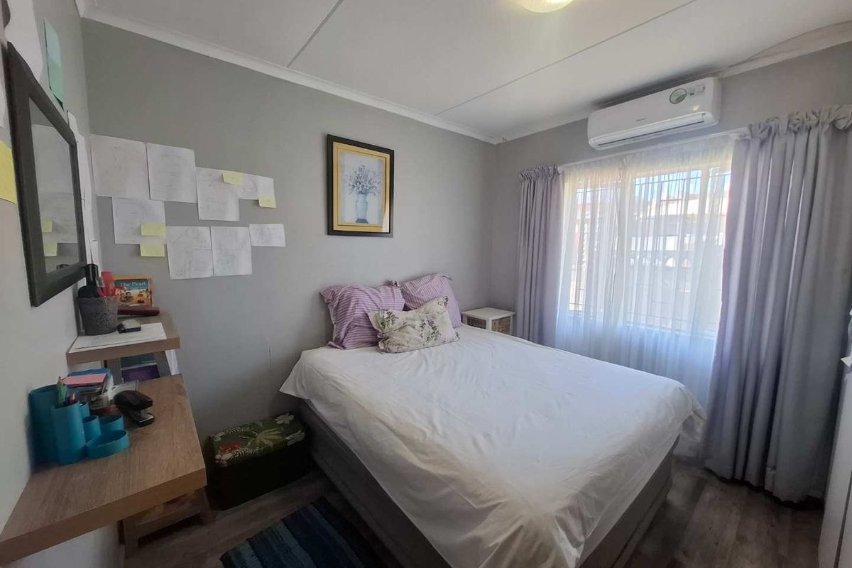 A functional bedroom featuring wood-look flooring, a wall-mounted air conditioning unit, and a window with curtain treatments.