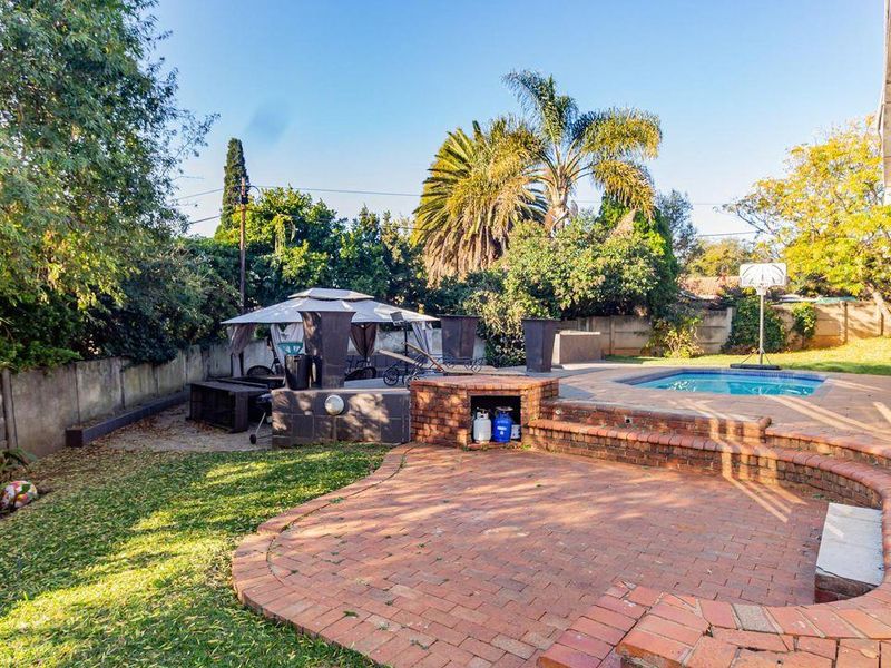 Outdoor entertainment area featuring a swimming pool, brick-paved patio, and a built-in braai, set within a private garden with perimeter walling.