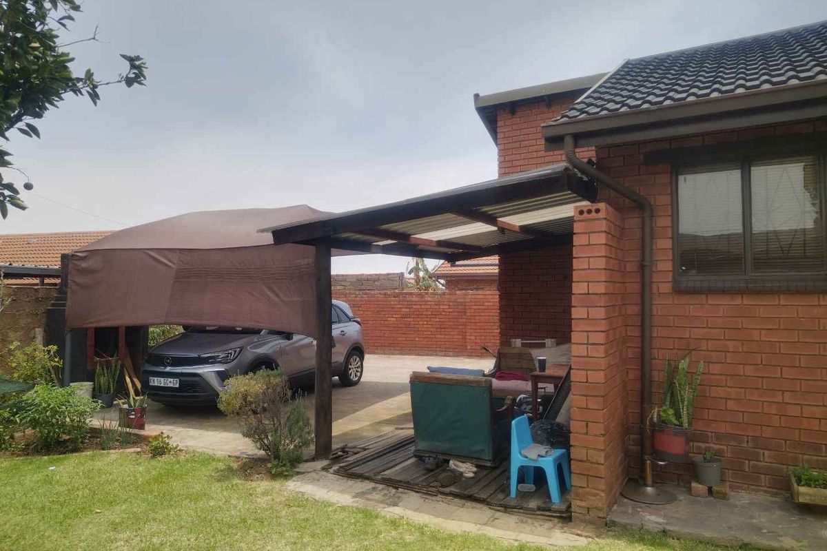 A rear exterior view featuring a brick facade, a covered patio area with timber decking, and an adjacent carport structure.
