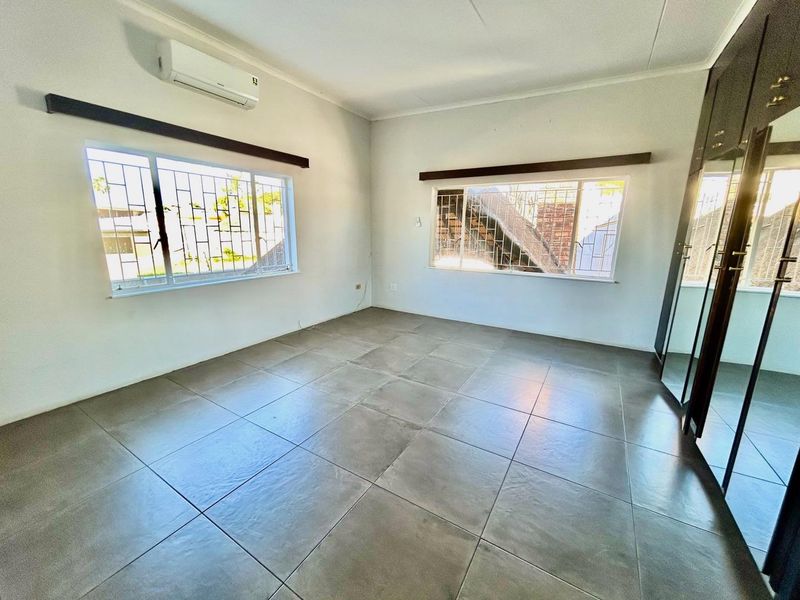 Spacious bedroom featuring large tiled flooring, built-in cupboards, and a wall-mounted air conditioning unit with security bars on the windows.
