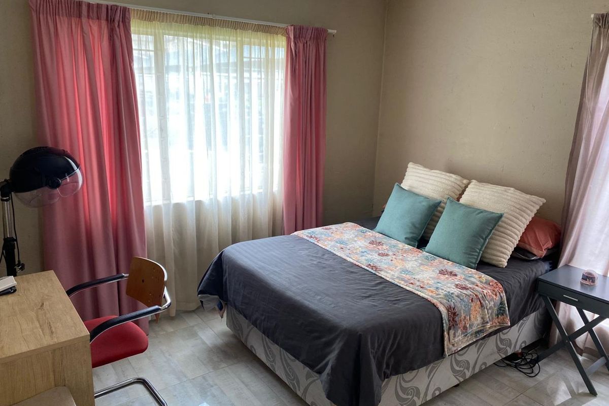A functional bedroom featuring tiled flooring and large windows with curtain rails, providing a neutral base for personal styling.