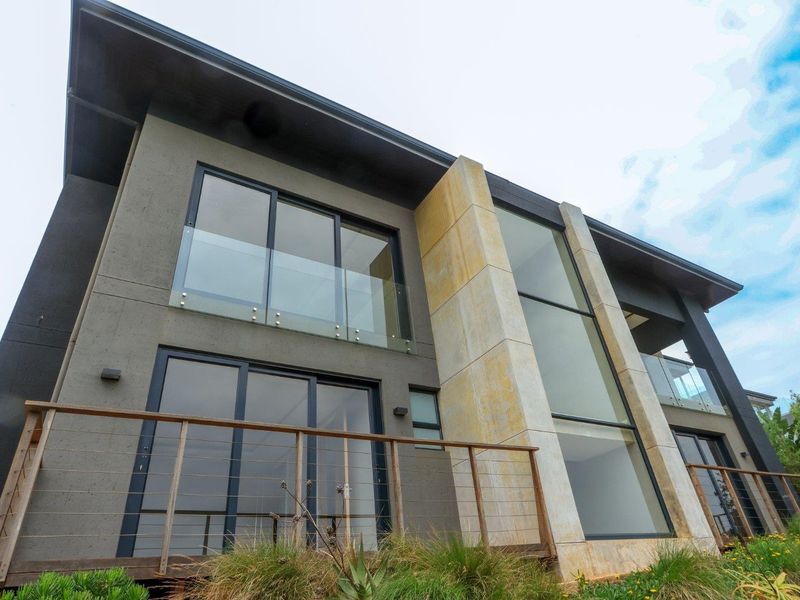 Modern multi-story rear facade featuring large glass sliding doors, stone feature wall, and timber decking with cable railings.