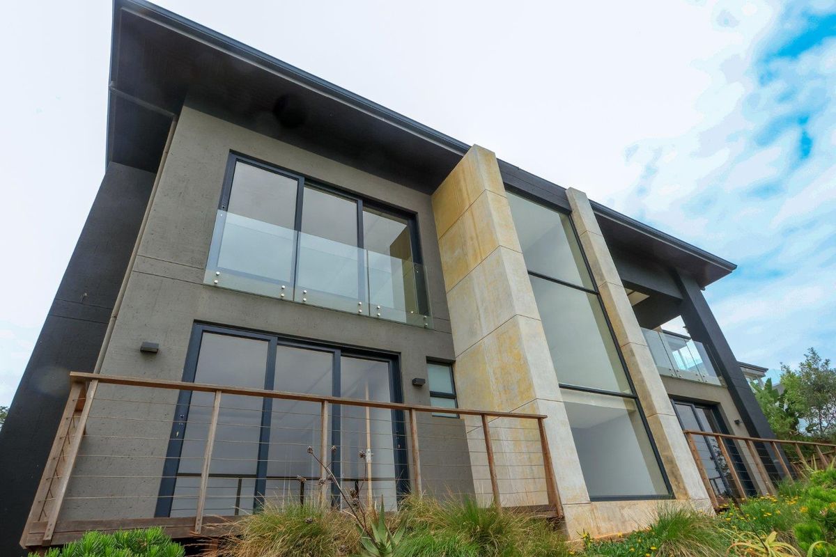 Modern multi-story rear facade featuring large glass sliding doors, stone feature wall, and timber decking with cable railings.